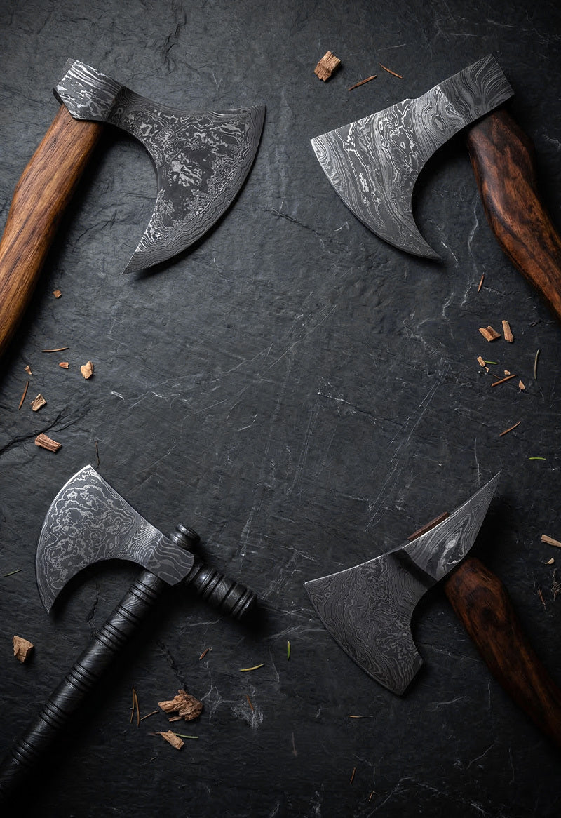 andmade Damascus steel axes and hatchets with wood and paracord wrapped handles arranged on dark stone surface – JW Steel Crafts custom forged axe and hatchet collection
