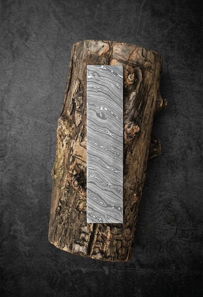 Handmade Damascus steel bar billet with twist pattern resting on raw wood log for knife and axe making – JW Steel Crafts custom Damascus steel bar stock supply