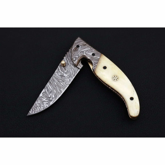 Studio-style product image of a handcrafted Damascus steel folding knife partially open, featuring a curved cream bone handle with brass accents and visible rivets, a patterned Damascus drop-point blade with thumb stud, displayed on a matte black background by JW SteelCrafts.