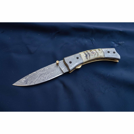 Custom Damascus steel folding knife with patriotic red white and blue handle, star inlay grip and etched blade displayed in hand during finishing stage