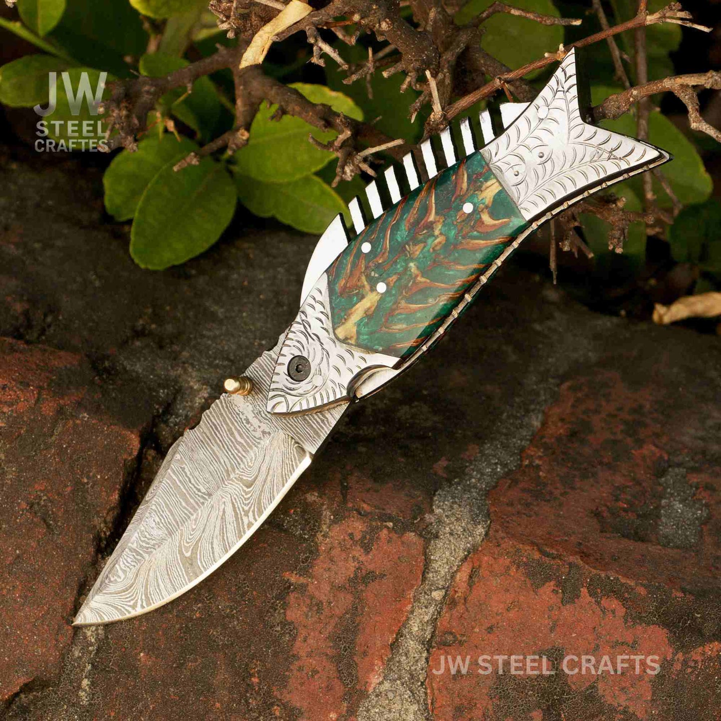 Decorative folding knife with a detailed blade on a natural background, branded 'JW Steel Crafts'.
