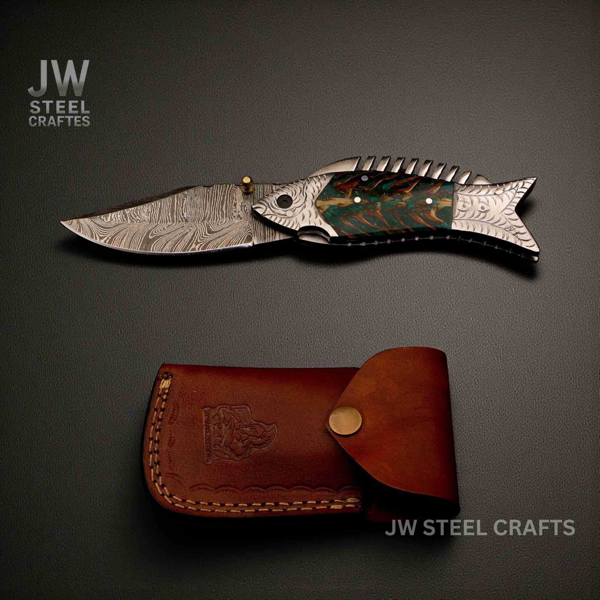 Folding knife with decorative handle and leather sheath on a dark background, branded 'JW Steel Crafts'.