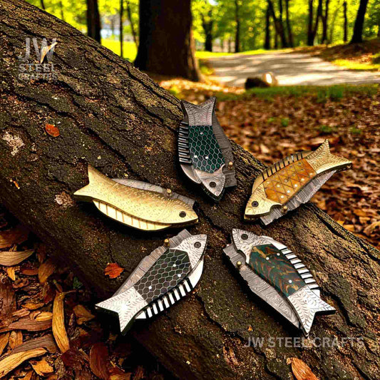 Fish folding knife with decorative steel blade and mixed handle variations displayed on a forest log by JW SteelCrafts.