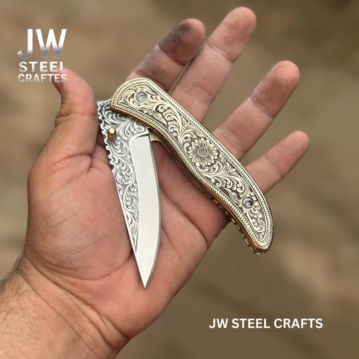 Hand-engraved brass handle folding knife by JW SteelCrafts displayed open in hand, featuring floral engraved brass scales and a hand-engraved stainless steel blade