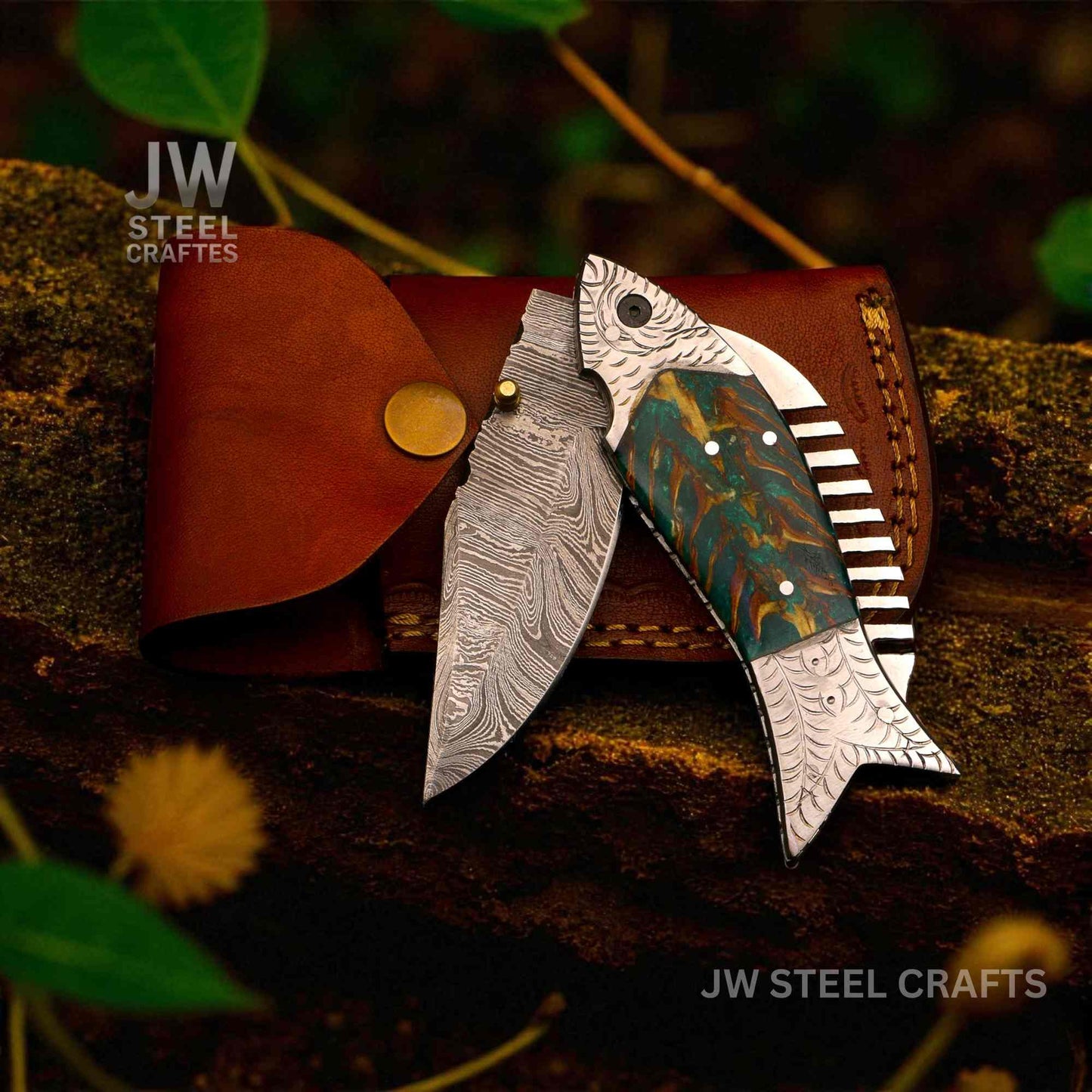 Decorative knife with artistic blade design on a leather sheath against a natural background, branded 'JW Steel Crafts'.