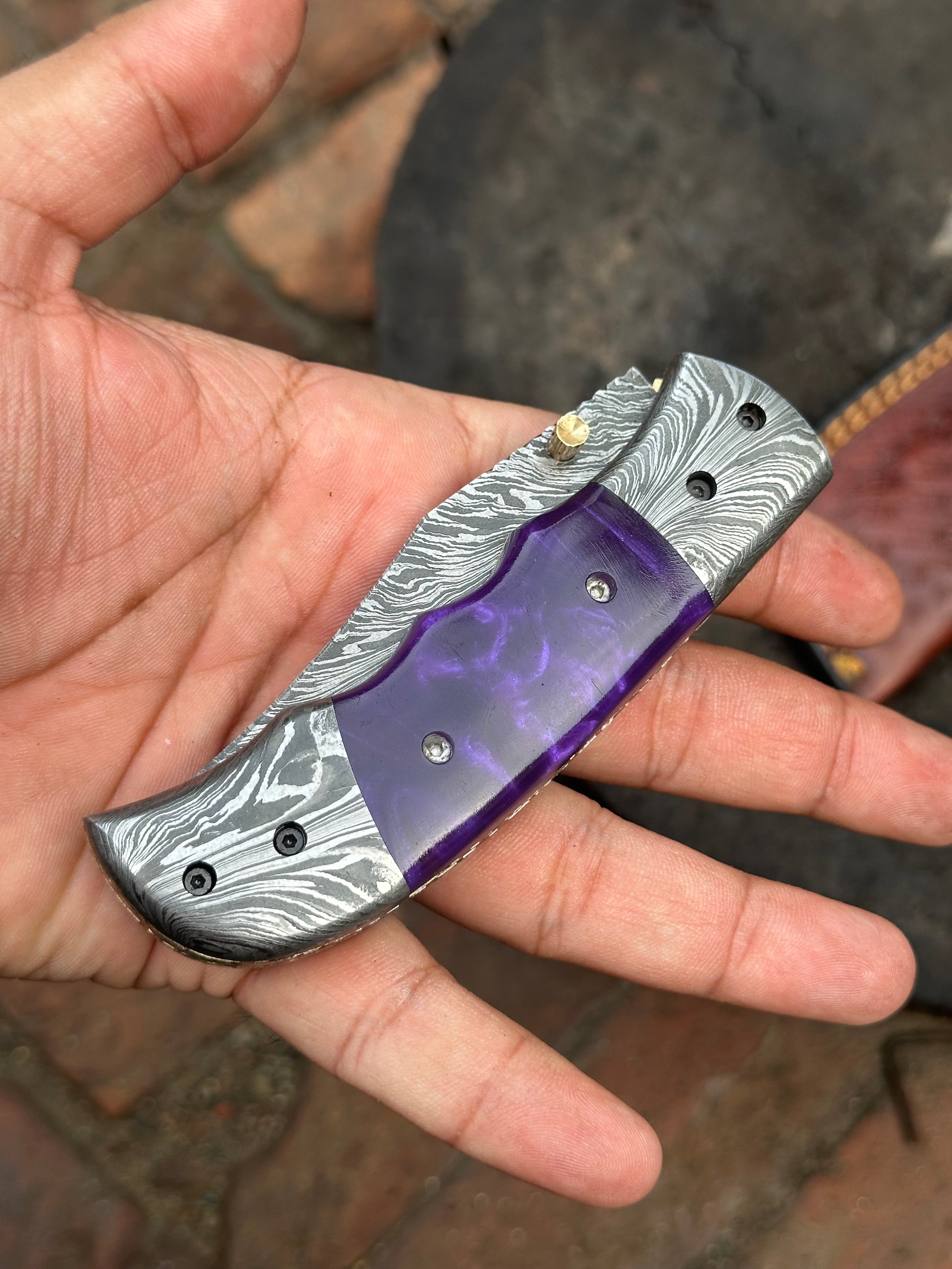 Folding knife with purple blade and silver handle held in a hand