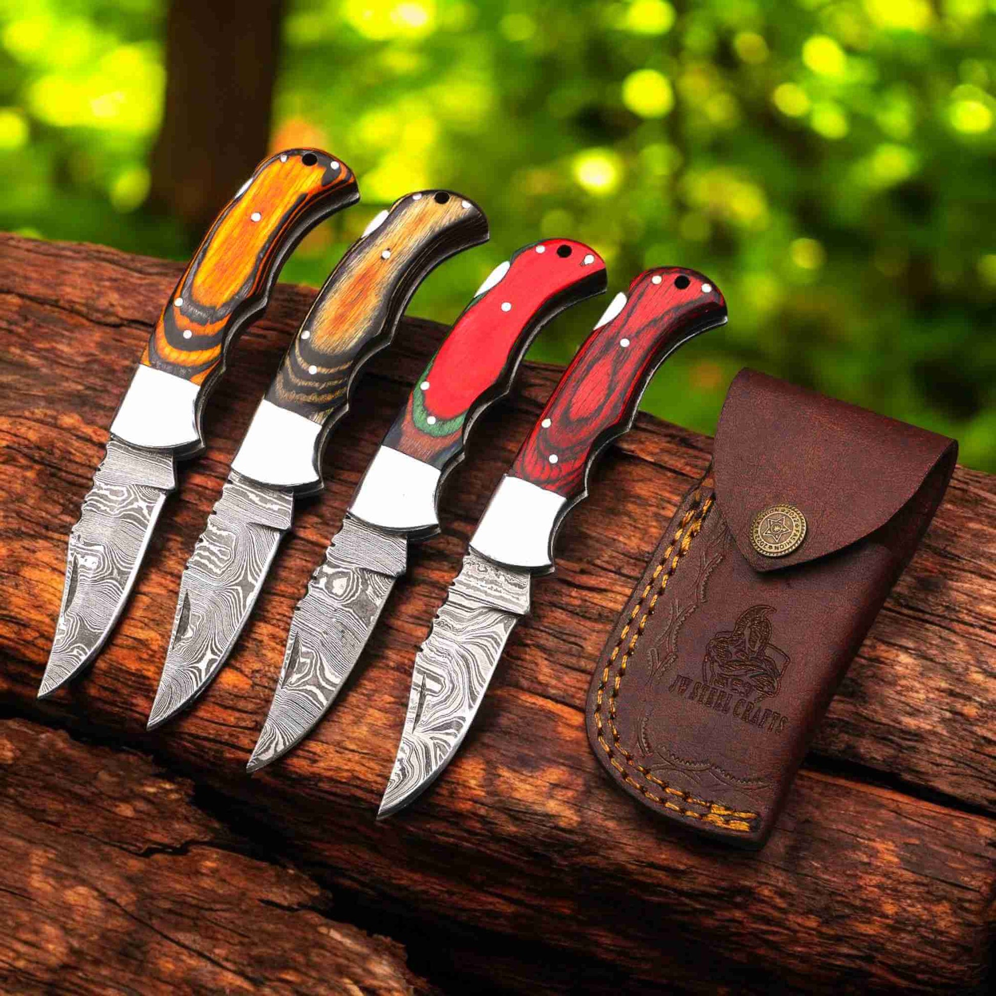 Four handcrafted Damascus steel fixed blade knives by JW SteelCrafts displayed on a wooden log, featuring colorful layered wood handles in orange, brown, red, and dark red tones, paired with a brown leather sheath embossed with the JW SteelCrafts logo