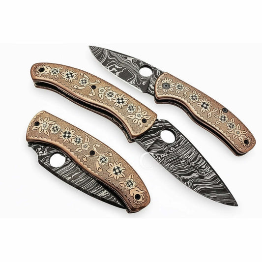 Studio image of three handcrafted Damascus steel folding knives with engraved floral-pattern wooden handles, compact curved blades with visible Damascus wave patterns, and thumb-hole openings, arranged on a clean white background by JW SteelCrafts.