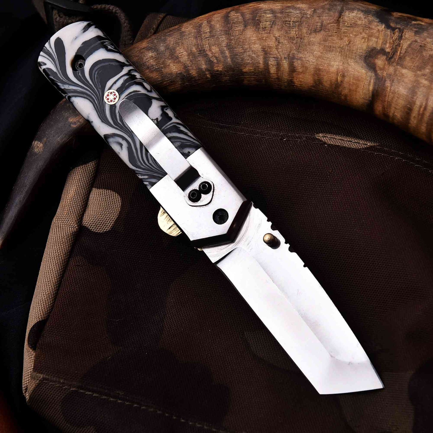 Stainless steel folding knife with marble resin handle and liner lock, displayed open on rugged outdoor gear