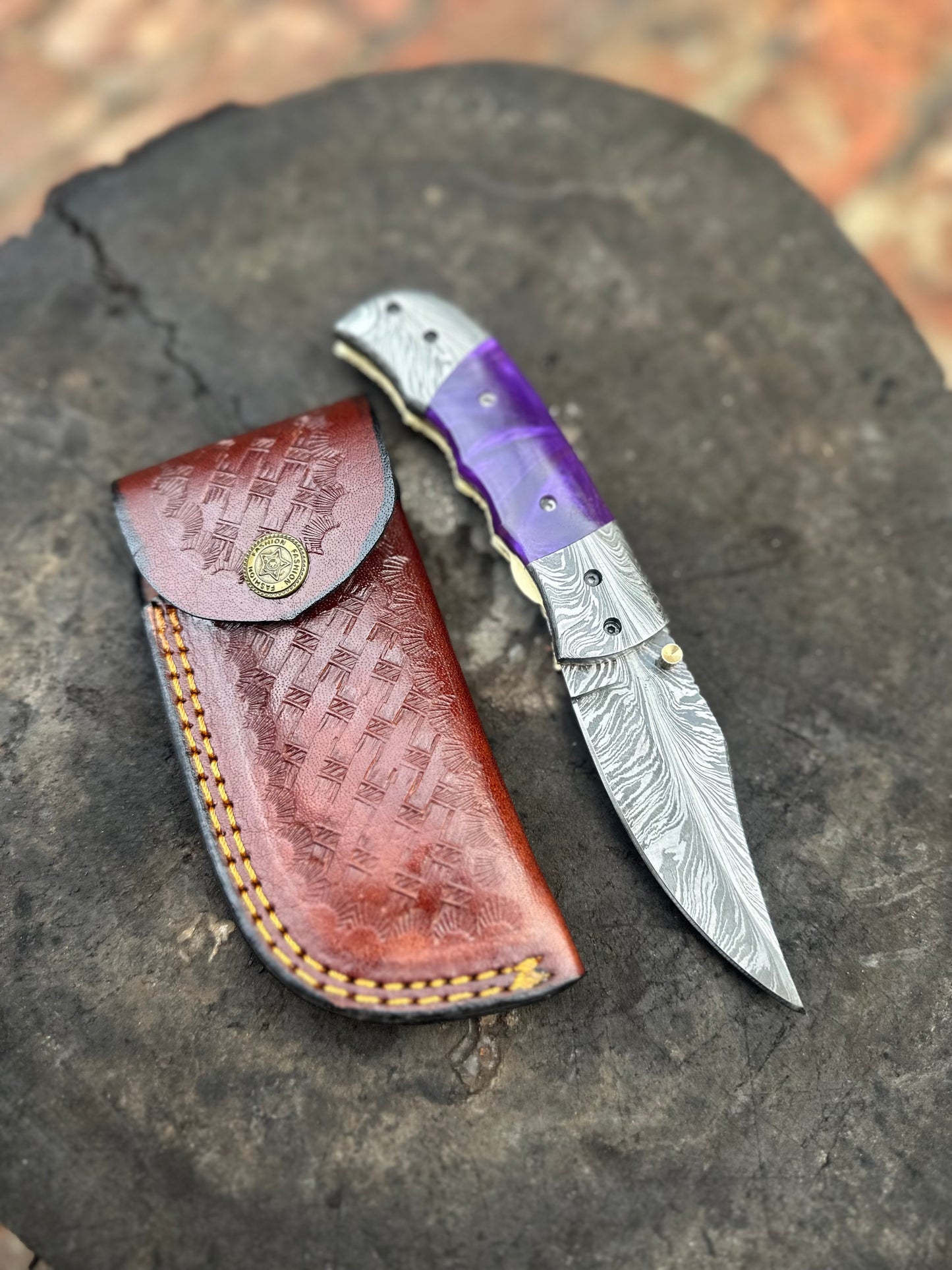 Knife with purple handle and silver blade on a leather sheath against a textured surface