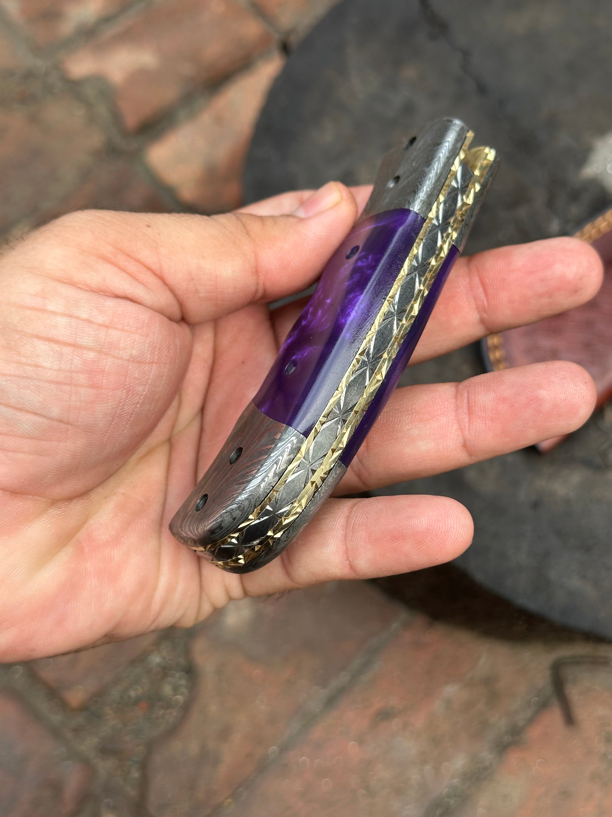 Hand holding a purple and gold object with intricate design on a textured surface