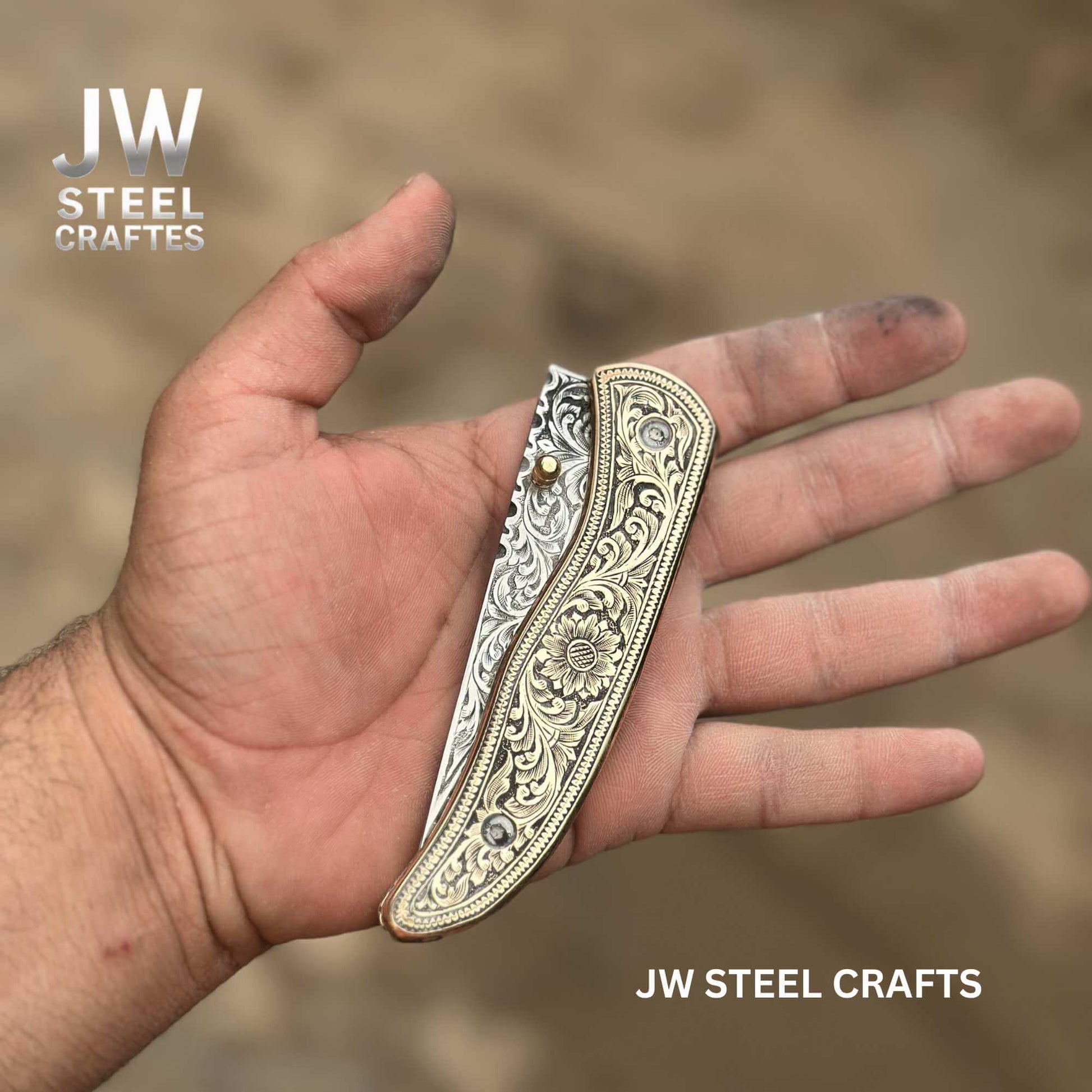 Partially opened hand-engraved brass handle folding knife by JW SteelCrafts, featuring detailed floral engraving on the handle and engraved stainless steel blade, displayed in hand