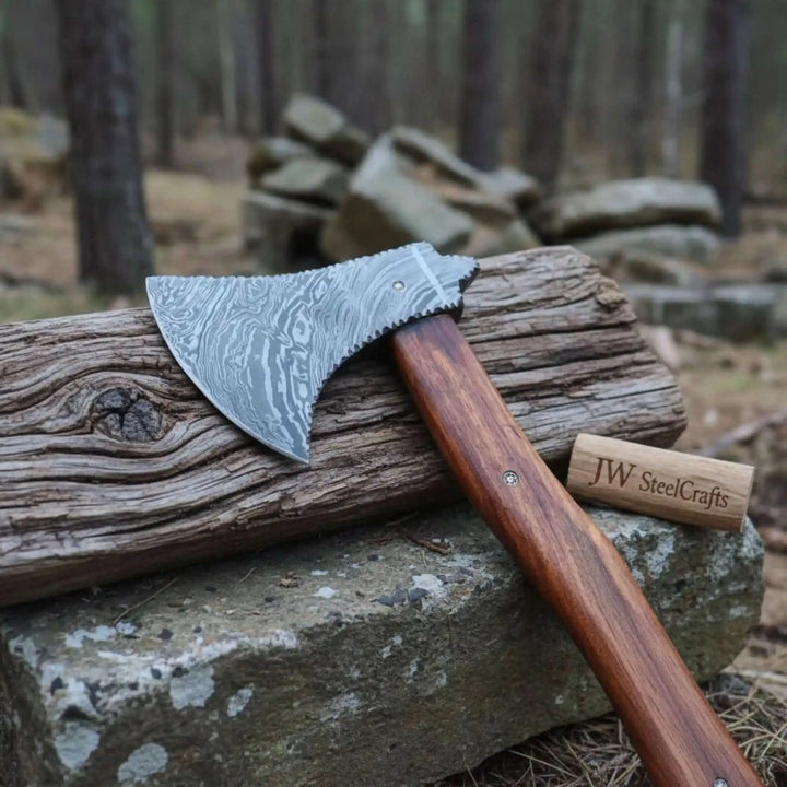     Branded custom camping hatchet featuring patterned Damascus steel and rich wooden handle displayed in a woodland environment.