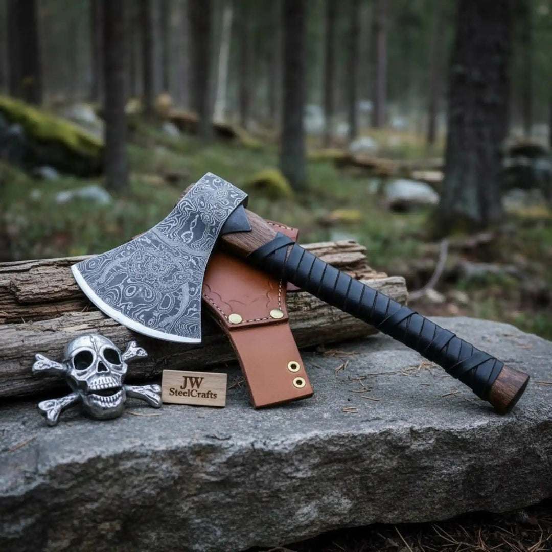     Cragthorn custom bushcraft hatchet with etched steel head and wrapped wooden grip positioned on a natural stone platform in woodland scenery.