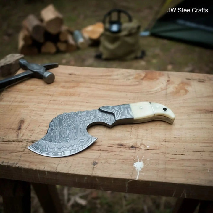     Cedarcrest custom camping knife with curved Damascus blade and ergonomic ivory handle resting on a rugged wooden table outdoors