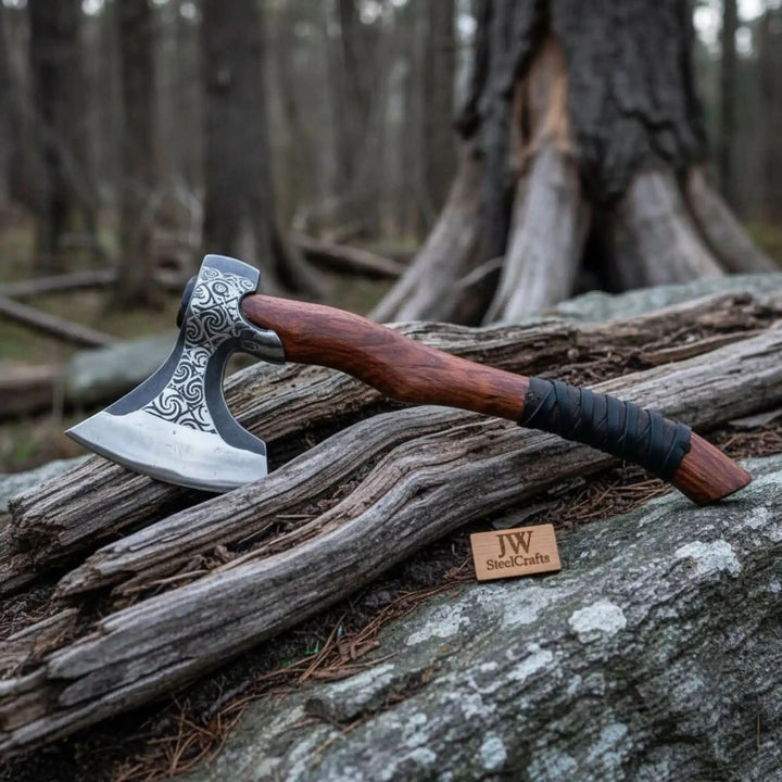    Blackthorn Nordic bushcraft axe featuring ornate etched blade and wrapped wooden grip in rugged woodland environment.