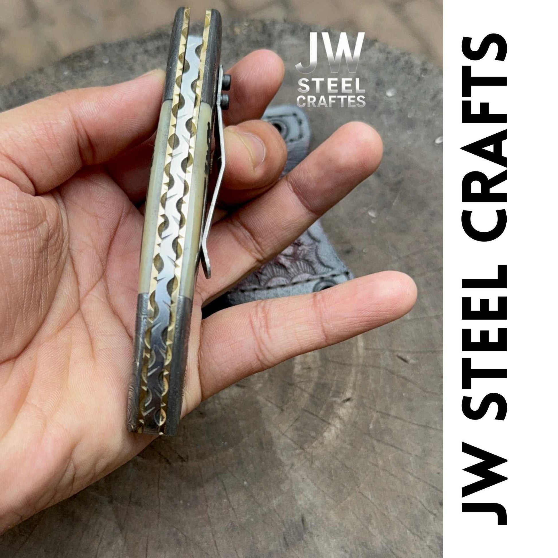 Hand holding a metal tool with 'JW Steel Crafts' branding on a concrete surface.