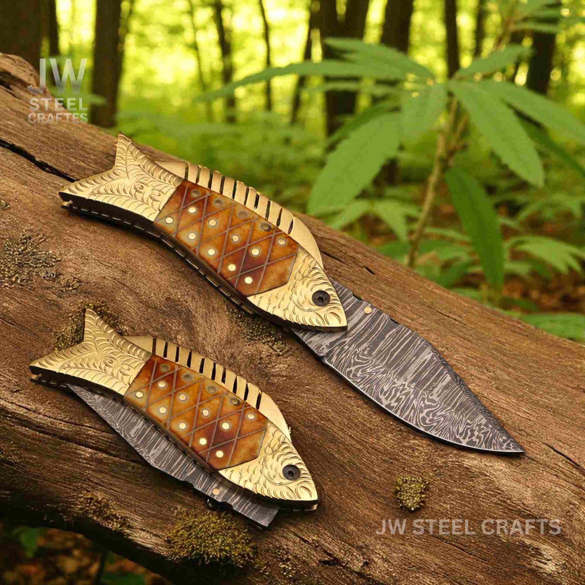 JW SteelCrafts handmade fish-shaped Damascus steel folding knife with engraved brass handle and natural bone inlay, displayed open and closed on a wooden log in a forest setting.