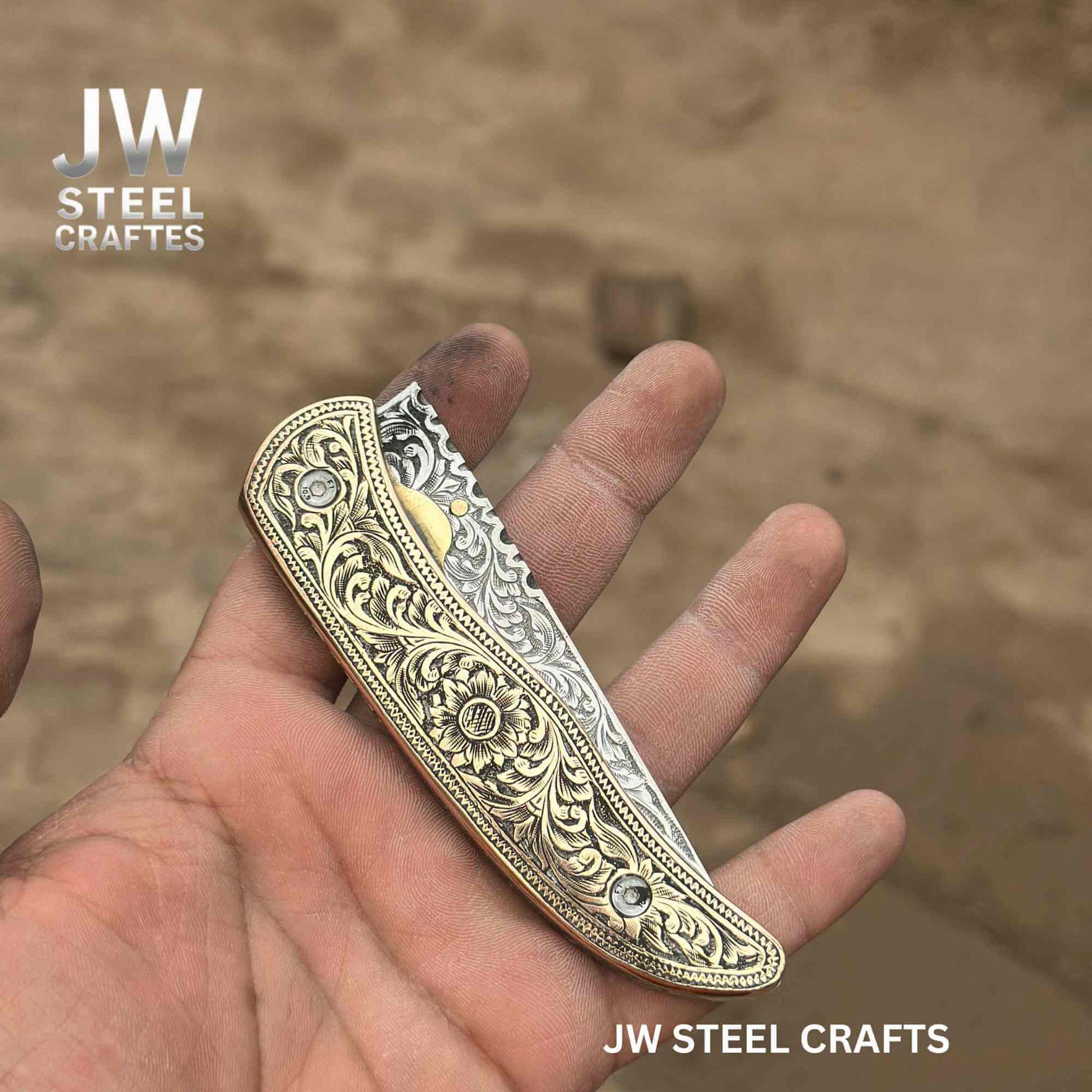 Closed view of a hand-engraved folding knife by JW SteelCrafts, showcasing an engraved brass handle with floral detailing and a partially visible hand-engraved stainless steel blade, held in hand