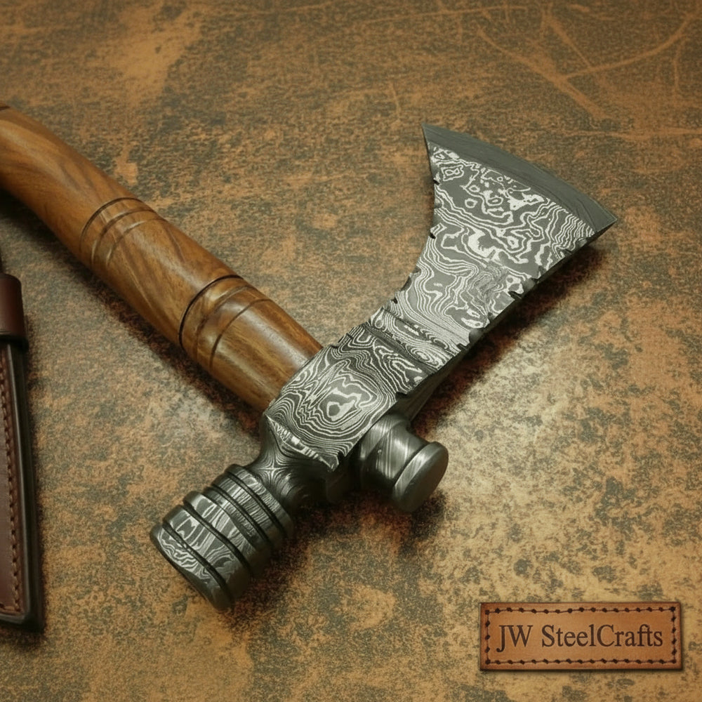     Drakewood handcrafted wilderness axe with engraved Damascus steel head and curved wooden handle at sunset campfire.
