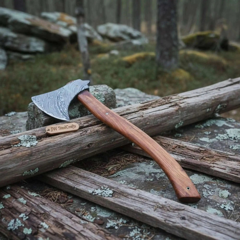     Detailed forged Damascus hatchet resting on stone and weathered log with artisan wooden handle in forest scenery.