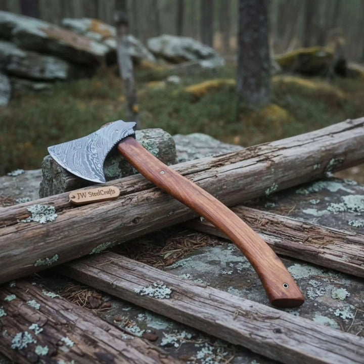    Detailed forged Damascus hatchet resting on stone and weathered log with artisan wooden handle in forest scenery.