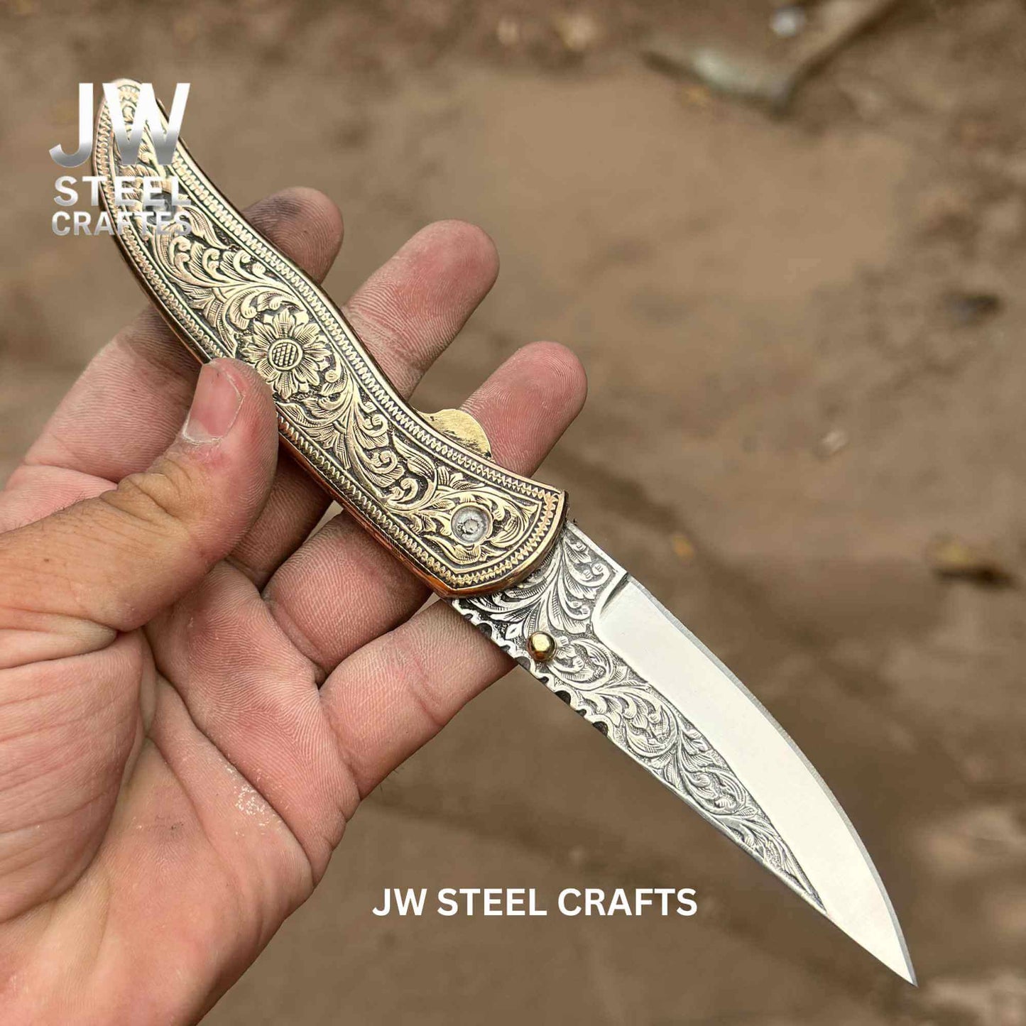 Hand-engraved brass handle folding knife by JW SteelCrafts displayed open in hand, featuring intricate floral engraving on the brass scales and detailed hand-engraved stainless steel blade with liner lock