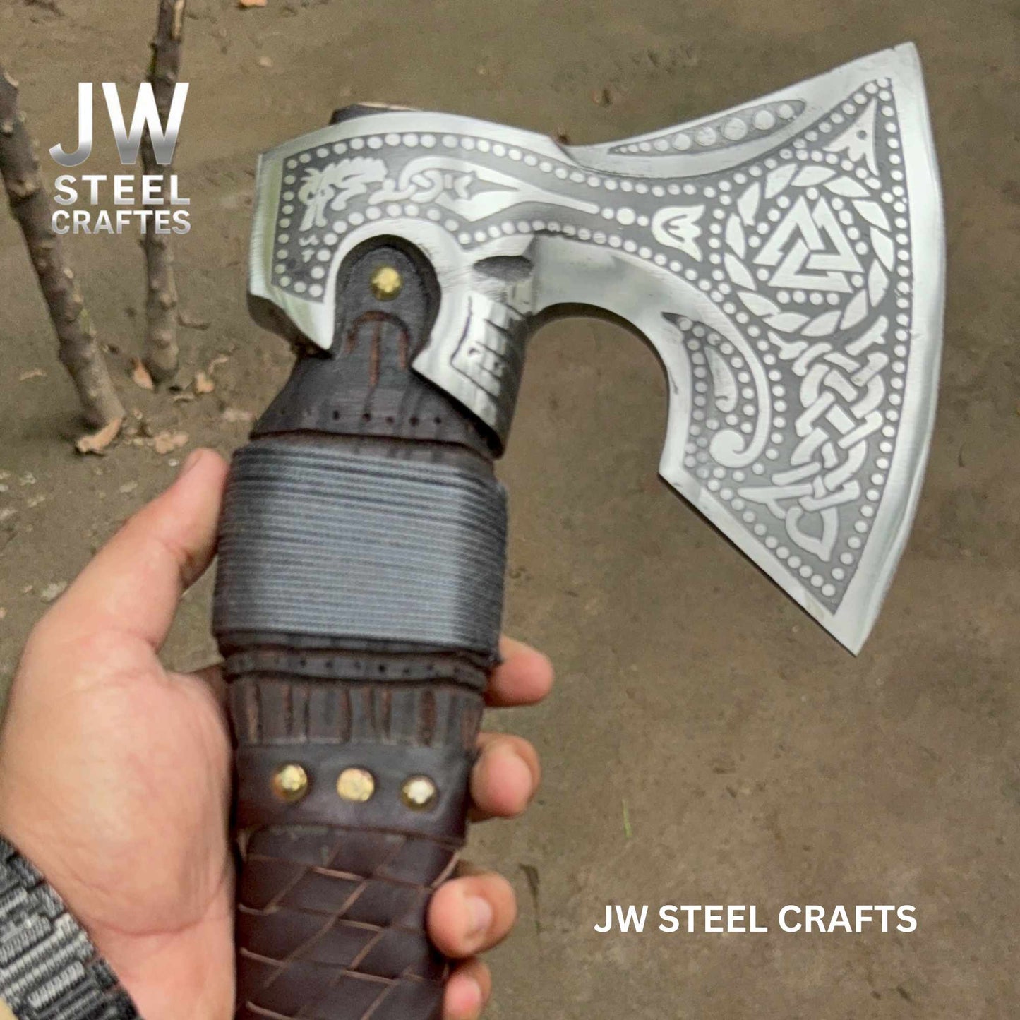 Decorative axe with intricate designs held by a hand, branded 'JW Steel Crafts'.