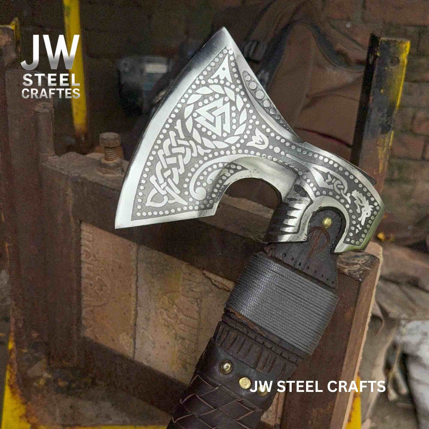 Decorative axe with intricate patterns on a wooden stand, branded 'JW Steel Crafts'.