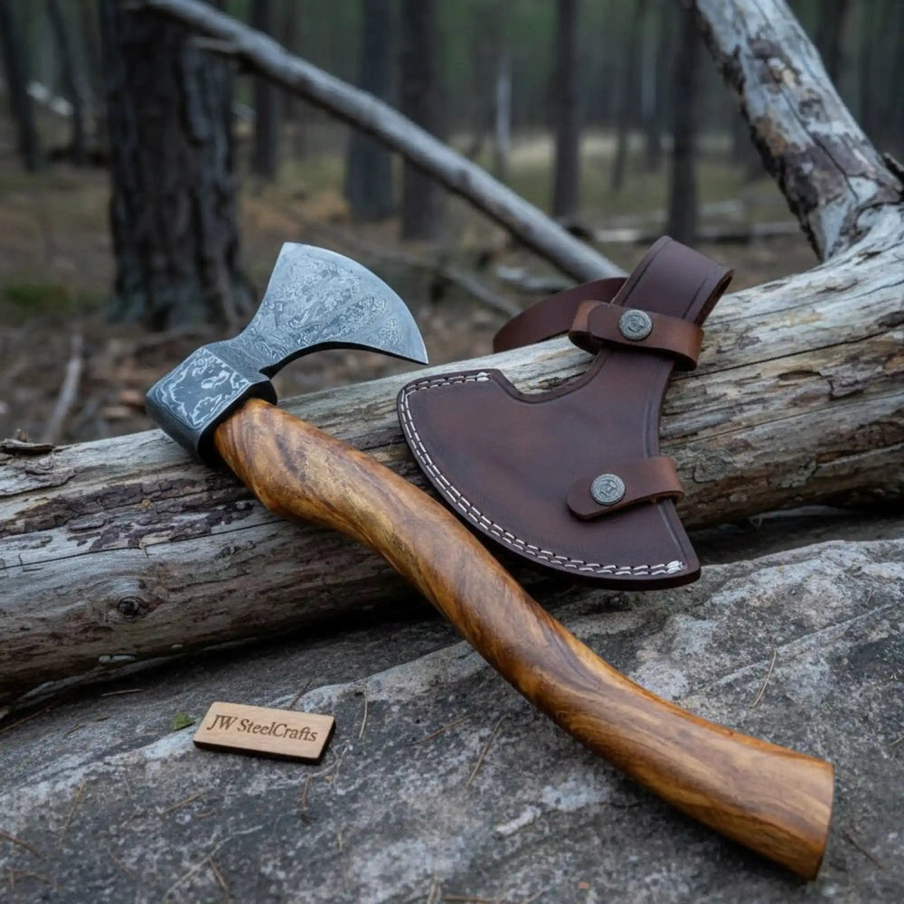    Evergrove artisan Damascus axe with curved wooden handle and detailed steel etching posed among mossy outdoor scenery.
