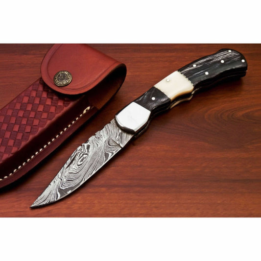 Handcrafted Damascus steel folding pocket knife with a patterned blade and black wood handle featuring a light bone inlay and metal bolster, displayed on a rich wooden surface to highlight craftsmanship by JW SteelCrafts.