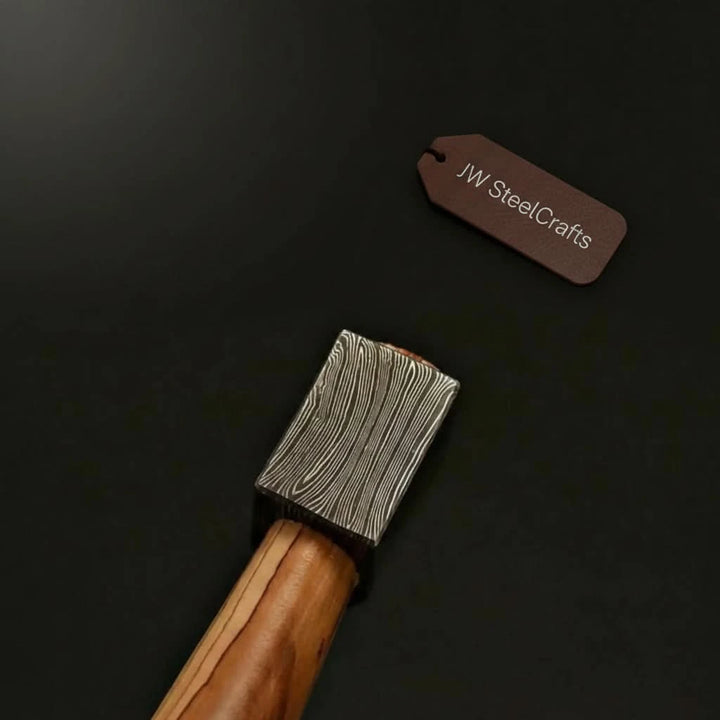     Ivoryridge artisan Damascus steel camp axe with compact rectangular blade and natural wood handle photographed outdoors.
