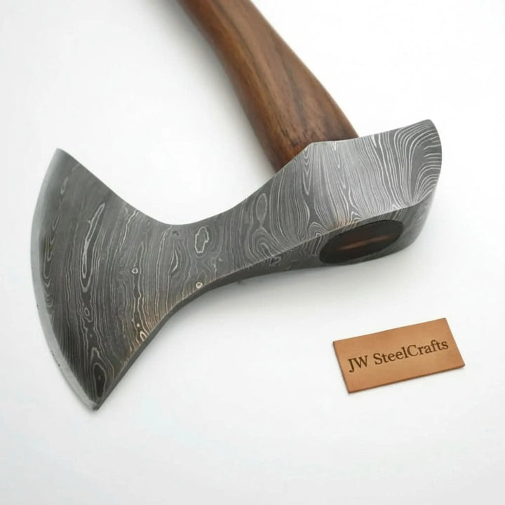     Hearthvale handmade camping axe with minimalist curved blade and smooth wooden handle resting on stacked stone slabs.