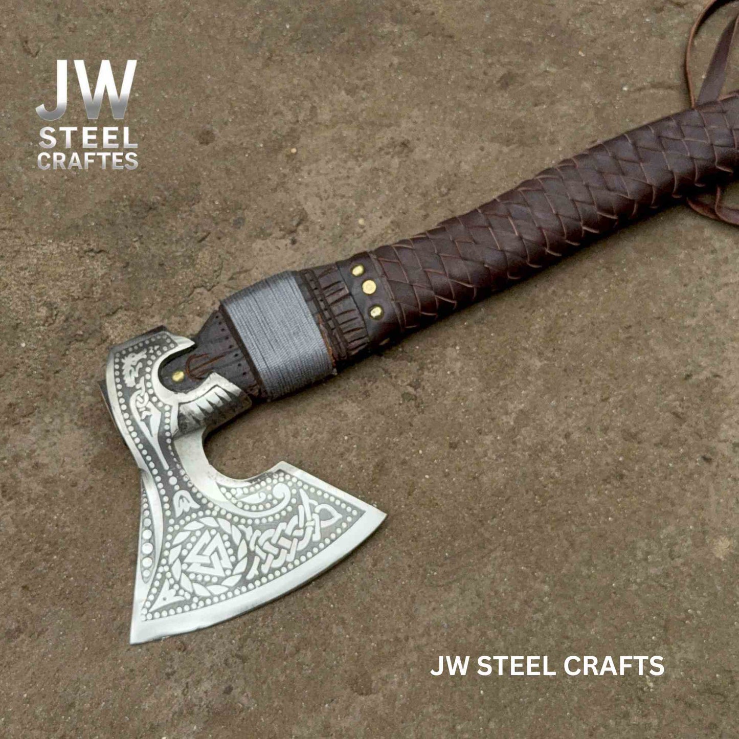 Decorative axe with leather handle on a textured surface, branded 'JW Steel Crafts'.