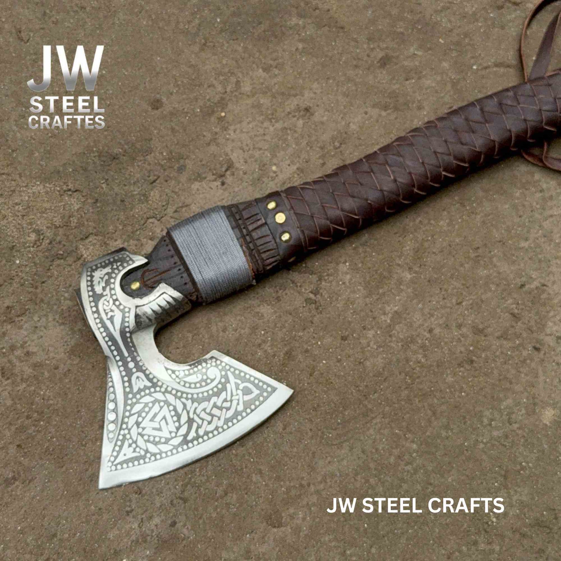 Decorative axe with leather handle on a textured surface, branded 'JW Steel Crafts'.