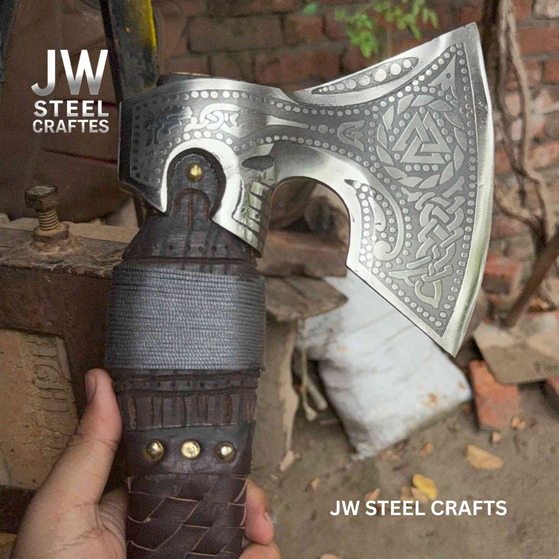 Decorative axe with intricate patterns held by a hand, branded 'JW Steel Crafts'.