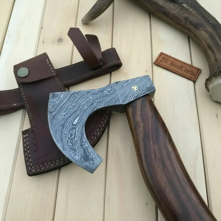     Jadecrest handcrafted outdoor survival axe accompanied by a stitched leather sheath on stone and timber in nature.