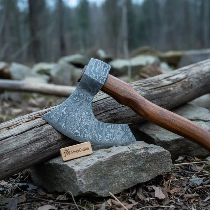     Moonridge artisan Damascus bearded hatchet featuring detailed steel wave patterns and rustic outdoor presentation.