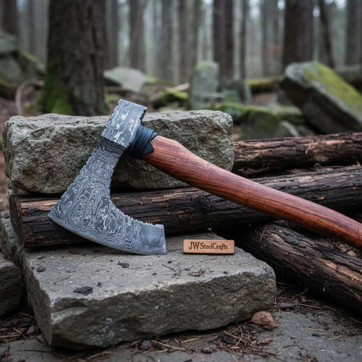     Handcrafted wilderness axe featuring layered Damascus steel blade and dark walnut wood handle displayed on rugged outdoor stones and timber.