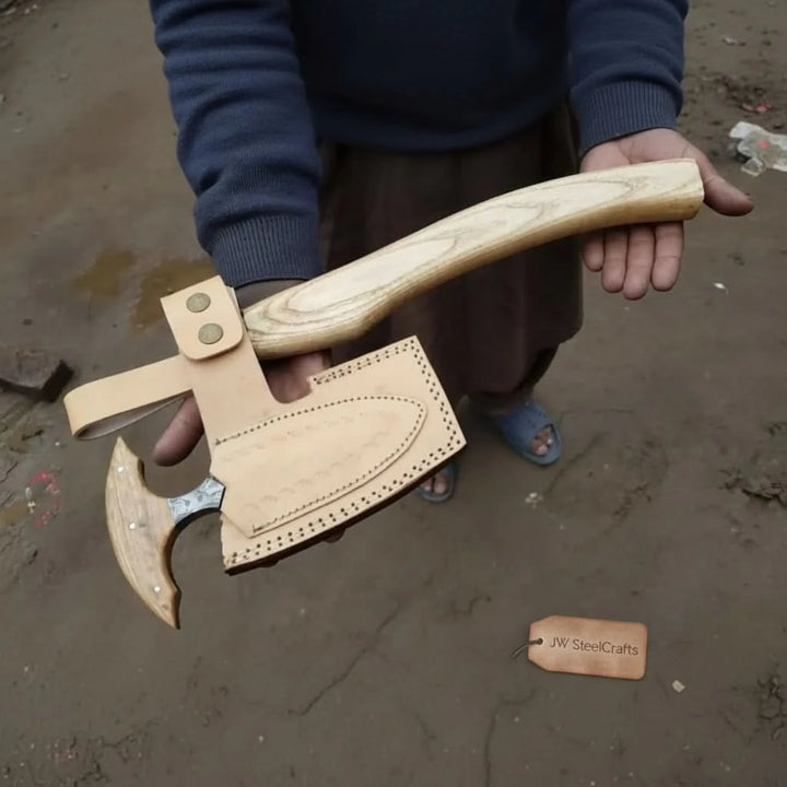     Pinehollow handcrafted Damascus survival hatchet paired with natural leather sheath and weathered woodland logs.