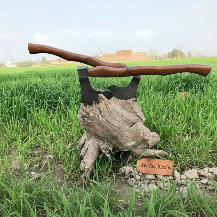     Outdoor bushcraft hatchet featuring layered Damascus steel blade and handcrafted wooden handle resting on rugged tree roots and grass.