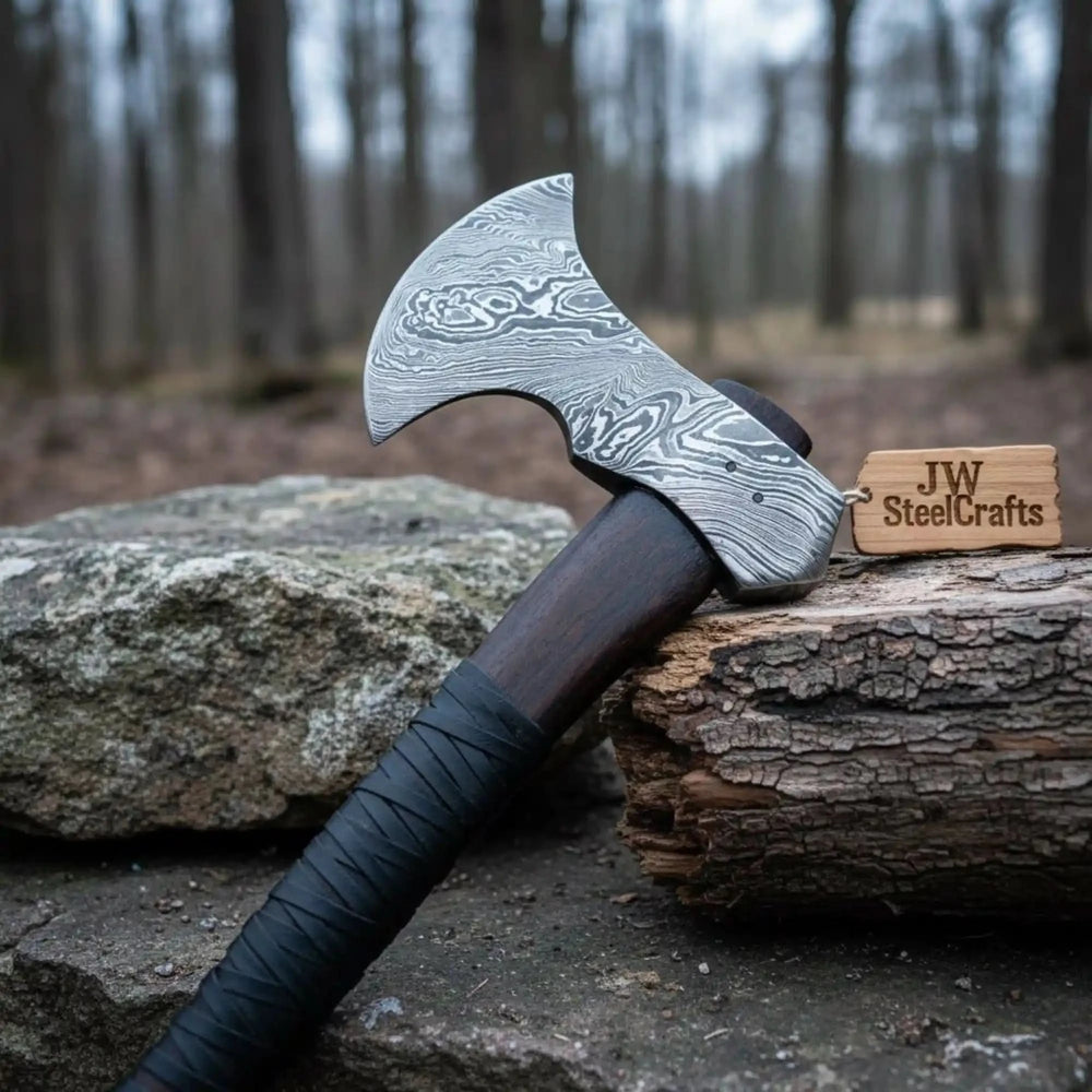     Stonebark premium Damascus axe with polished layered steel edge and dark wrapped handle in rustic camp environment.