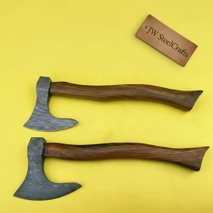     Thornvale artisan wilderness axe pair resting on weathered timber with contrasting Damascus steel blade finishes.