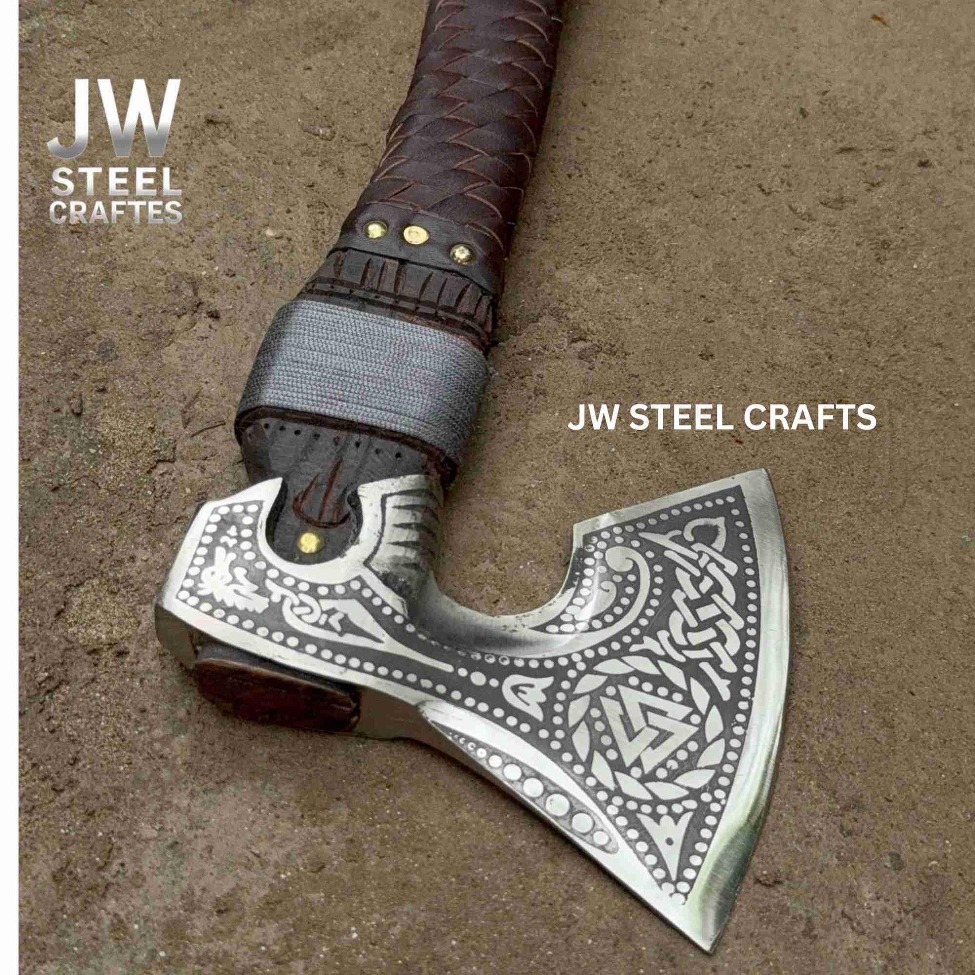 Decorative axe with engraved design on a brown surface, branded 'JW Steel Crafts'.