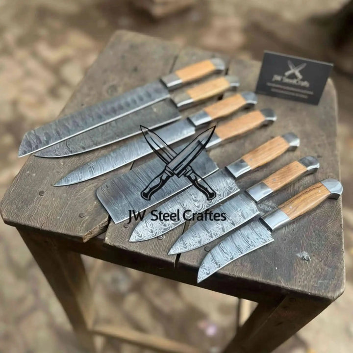 A set of handcrafted Damascus steel chef knives with wooden handles displayed on a rustic wooden stool, branded with the JW Steel Craftes logo