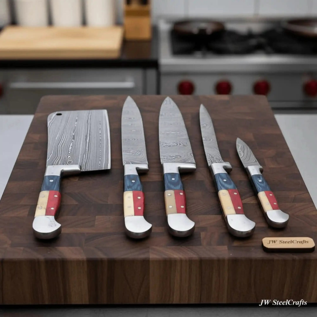Five handforged Damascus steel kitchen knives with bold Texas flag red white blue handles arranged in size order on a thick walnut butcher block with professional kitchen background
