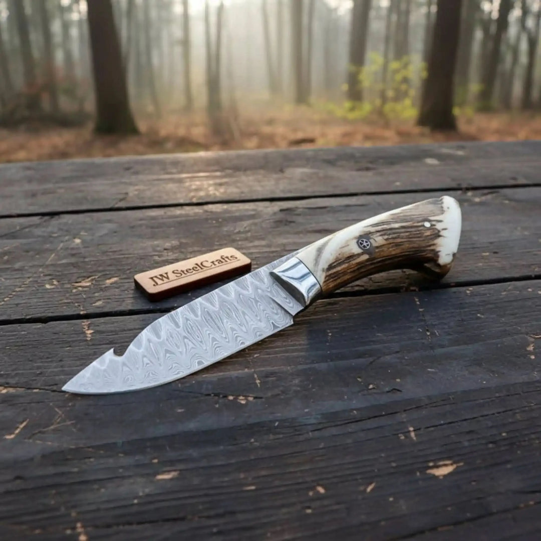 Stag antler handle Damascus gut hook knife with polished blade edge and JW SteelCrafts wooden tag.