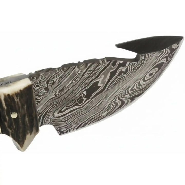 Curved Damascus gut hook knife on wood table with antler handle, gold rivets, and JW SteelCrafts tag.