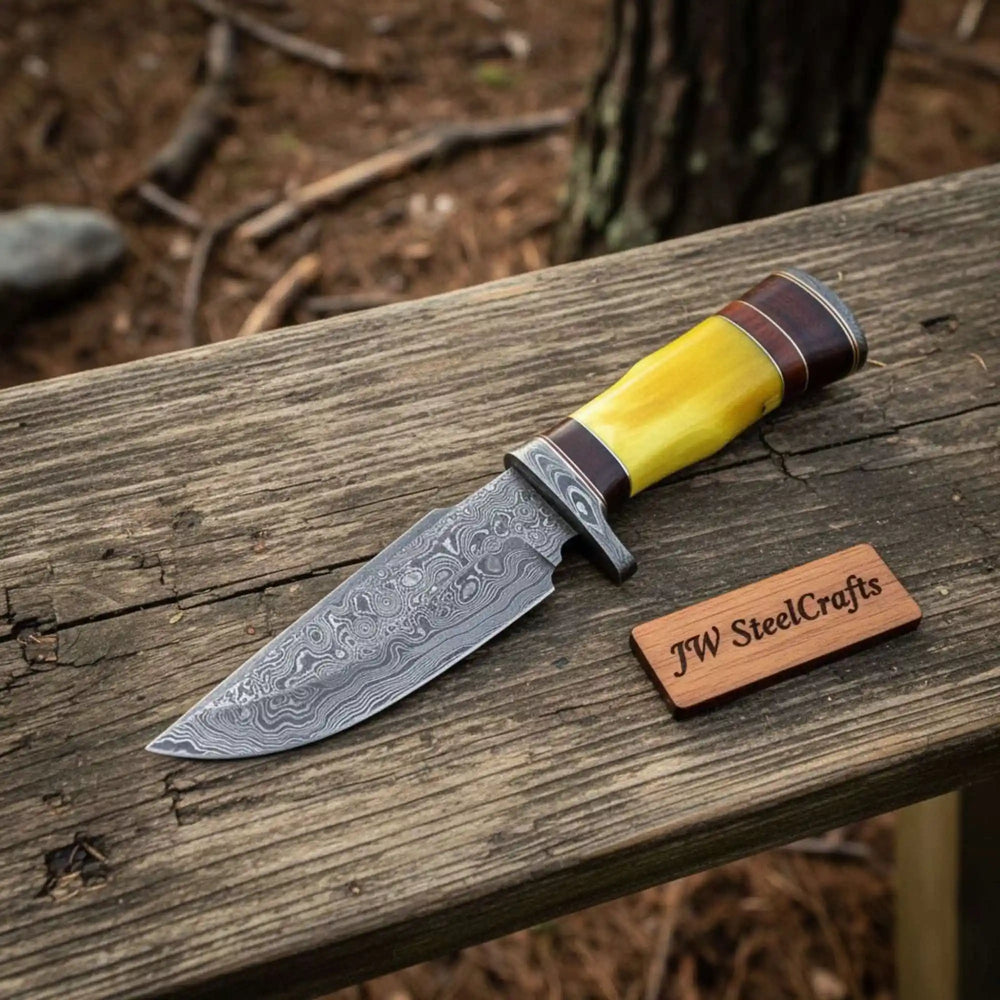 Sharp hunting knife with yellow handle, Damascus pattern blade, brown leather sheath, and outdoor wooden backdrop.