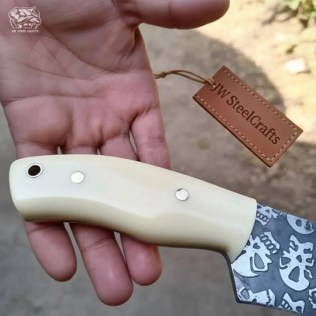Custom survival knife with skull pattern blade and ivory white scales displayed in rustic outdoor scenery.